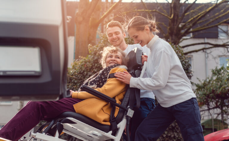 A carer hugging a woman in a wheelchair outside her home